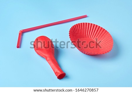 Red paper molds for baking muffins, balloon and straw lies on blue desk on kitchen. Close-up