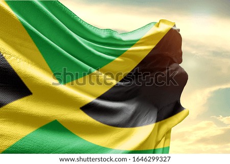 Waving Flag of Jamaica in Blue Sky. Jamaica Flag on pole for Independence day. The symbol of the state on wavy cotton fabric.
