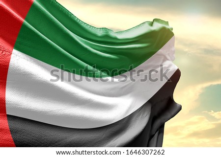 Waving Flag of United Arab Emirates in Blue Sky. UAE Flag on pole for Independence day. The symbol of the state on wavy cotton fabric.