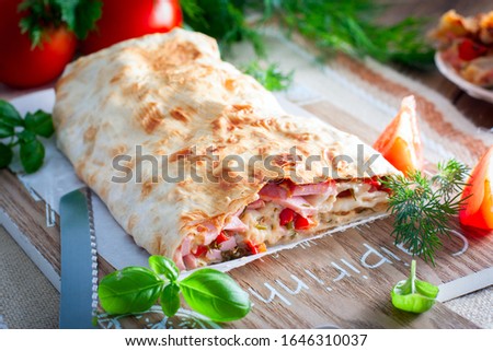 Baked pita roll with sausage and vegetables on a wooden board, selective focus