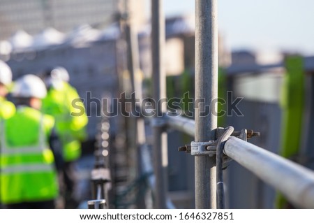 Architect on site Silhouette Construction workers on a scaffold. Extensive scaffolding providing platforms for work in progress. Men walking on roof surrounded by scaffold - Focus on scaffolding frame Royalty-Free Stock Photo #1646327851