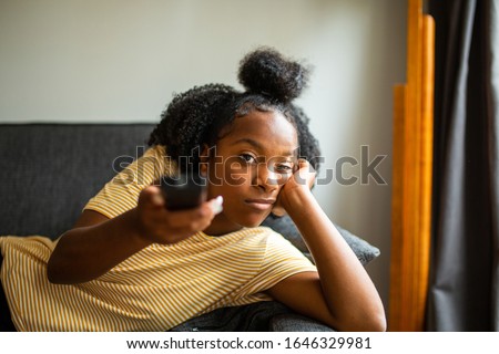 Portrait of bored african american girl on sofa pointing tv remote control