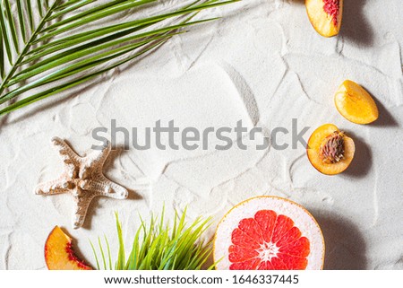 Charming beach. Bright fruits, a starfish, and palm leaves lie on the white sand. Close-up, top view, desktop wallpaper. Copyspace.