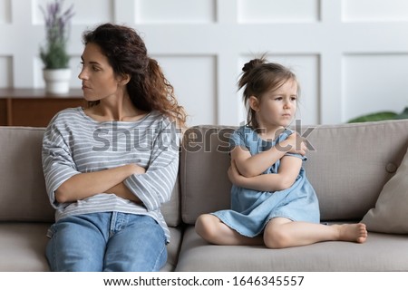 Stressed young mother sitting separately with offended little preschool daughter, ignoring each other in living room. Frustrated woman not talking to stubborn kid girl, family problems concept. Royalty-Free Stock Photo #1646345557