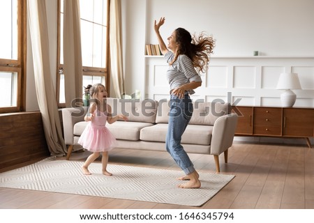 Full length overjoyed little preschool child girl in princess wear spending active weekend time with happy young mother. Crazy energetic family of two dancing together to music in living room. Royalty-Free Stock Photo #1646345794