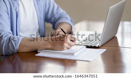 Close up of concentrated male student busy studying using laptop make notes in notebook, focused man worker employee write watching webinar or online training course on computer, education concept Royalty-Free Stock Photo #1646347051