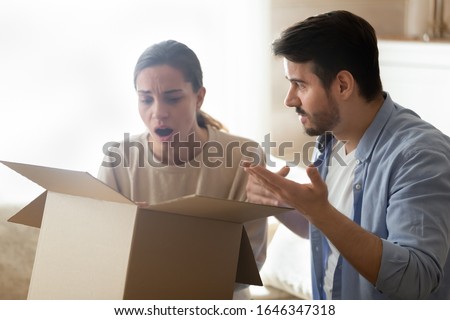 Disappointed man and woman unpack cardboard box shopping online frustrated by wrong bad quality order, upset young couple customers open post shipping parcel confused with internet purchase Royalty-Free Stock Photo #1646347318