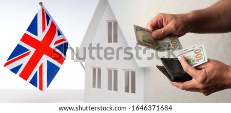 Hand with money on the background of a cottage with the flag of great Britain. Purchase of real estate in England. Payment for accommodation in London. Rental housing in the United Kingdom.