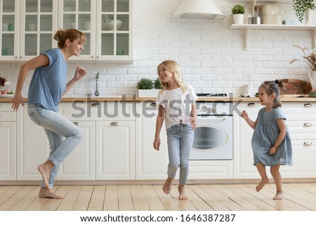 Overjoyed millennial mom or nanny dancing with little girls children in white modern kitchen, happy young Caucasian mother have fun involved in activity together with small daughters at home Royalty-Free Stock Photo #1646387287