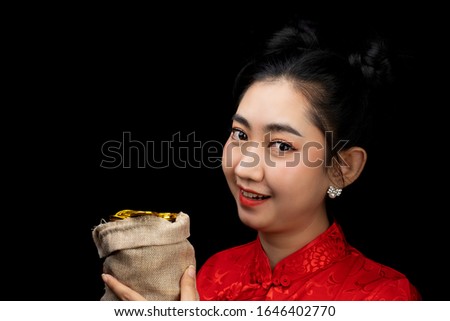 Portrait Asian young woman red dress traditional cheongsam holding a gold coin in a sack at the black background, China Girl, Concept Chinese New Year