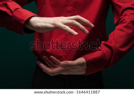 Close-up hands of an unidentified young man in a red shirt carefully hold an invisible object. Digital and graphic concept. Advertising space