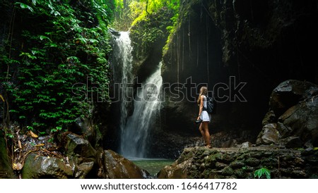Happy woman tourist to travel in wild trip hiking during vacation .Travel hiking. Woman art photographer works at camera on Bali, Indonesia. The Gitgit waterfall on the island of Bali
