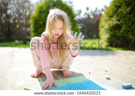 Cute little girl drawing with colorful chalks on a sidewalk. Summer activity for small kids. Creative leisure for family.
