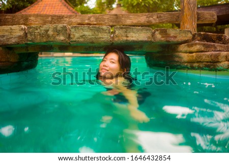 holidays lifestyle portrait of young beautiful and happy Asian Chinese woman in bikini enjoying vacation trip relaxed and blissful at tropical resort swimming pool in exotic tourism and wanderlust 