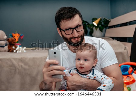 Father takes a selfie with his son on the phone. Baby looking at the camera, posing. Father and son concept.