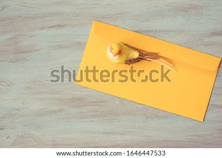 Yellow toy bird and colored envelopes for letters on wooden background. Easy abstraction for background. Copy space