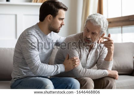 Young stressed man comforting irritated mature old father, sitting together on couch. Worried grownup son feeling sorry, asking forgiveness to angry offended unhappy middle aged hoary daddy. Royalty-Free Stock Photo #1646468806