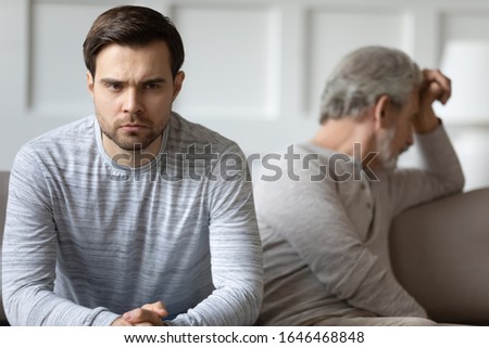 Focus on stressed angry young man sitting separate on couch with stressed offended middle aged father. Unhappy grownup son feeling irritated after argue quarrel with dad, generations gap concept. Royalty-Free Stock Photo #1646468848