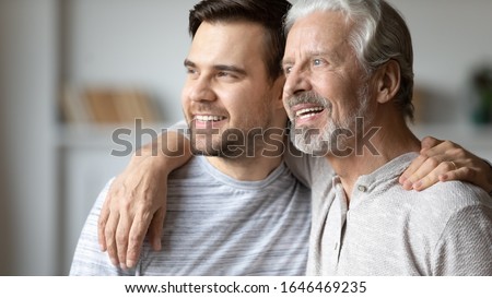 Head shot close up thoughtful dreamy positive two male generations family embracing, supporting each other, planning future. Happy young man looking at window with smiling older mature father.