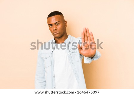 Young latin man isolated on beige background standing with outstretched hand showing stop sign, preventing you.