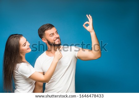 Beautiful young happy couple love smiling embracing point finger to empty copy space, man and woman smile looking up, isolated over blue background