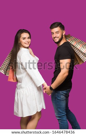 Happy couple with shopping bags, standing close to each other with smile. Caucasian models in love, holiday sales, shop, retail, consumer concept.