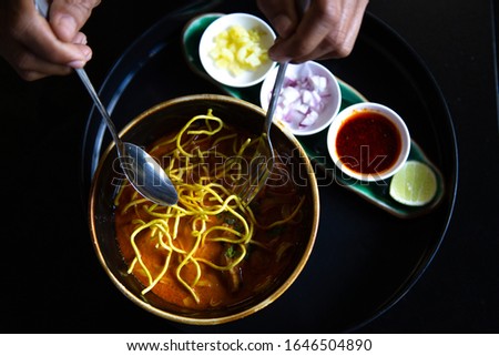closeup Hand Holding yellow noodles  spoon,Asian food  noodles  soup  in  bowl on the wooden table vegetable and ingredient,