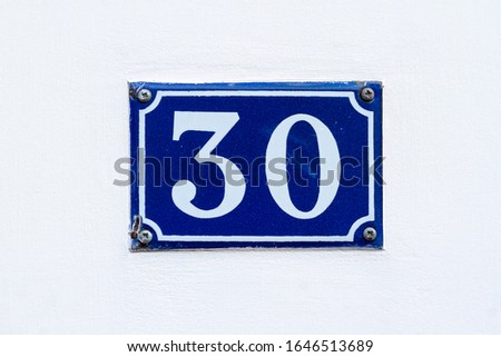 House number 30 on a blue enamel sign on a white wall