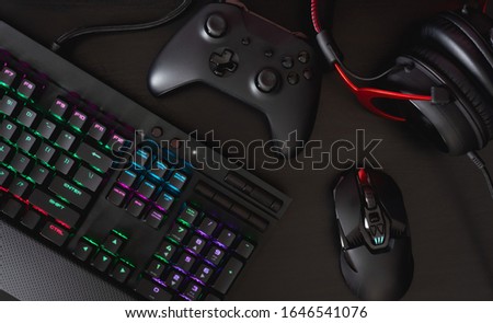 gamer workspace concept, top view a gaming gear, mouse, keyboard, joystick, headset, in ear headphone and mouse pad on black table background with copy space.