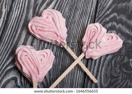 Delicate pink marshmallows in the shape of a heart on a stick. Several pieces lie on brushed pine boards painted in black and white.