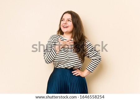 Young curvy woman laughs out loudly keeping hand on chest.