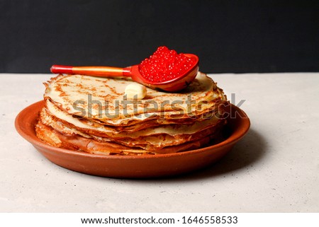 Traditional Shrovetide Maslenitsa Food. Crepes Or Pancakes With Red Salmon Caviar In Spoon On Clay Plate, Grey Table, Black Background. Side View. Copy Space.