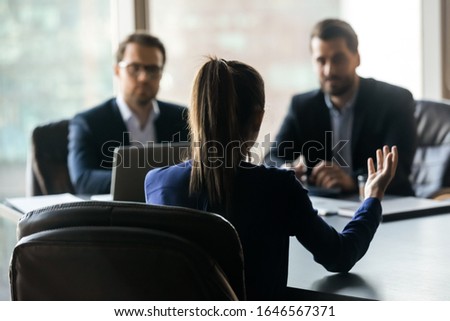 Hiring attractive woman applicant back sitting in front two HR businessmen. Candidate for work interview in office. Young female job seeker presenting herself to managers in suit. Royalty-Free Stock Photo #1646567371