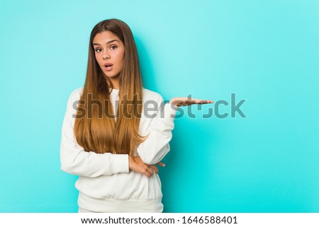 Young slim woman impressed holding copy space on palm.