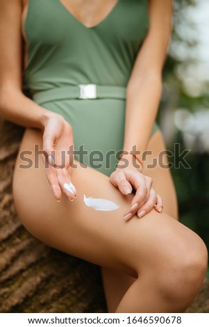 slim female in bikini applies moisturizer cream to body, girl with perfect slim body sit on exotic tropical tree in forest. concept of skin care , sun protection cosmetics, moisturizing, whitening