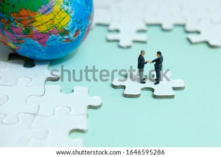 Business strategy conceptual photo - Miniature businessman make handshake partnership above jigsaw puzzle piece with globe