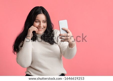 Selfie Time. Pretty Plump Girl Taking Self-Portrait On Smartphone, Isolated On Pink Background, Empty Space