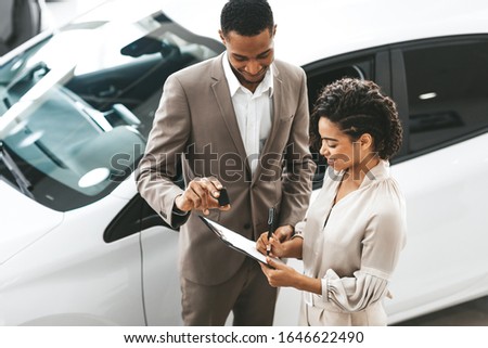 Afro Lady Buying New Car Signing Papers With Dealer Man Standing In Auto Dealership Store.