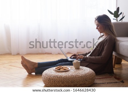 Young girl chatting with friends online, resting at home with laptop, empty space
