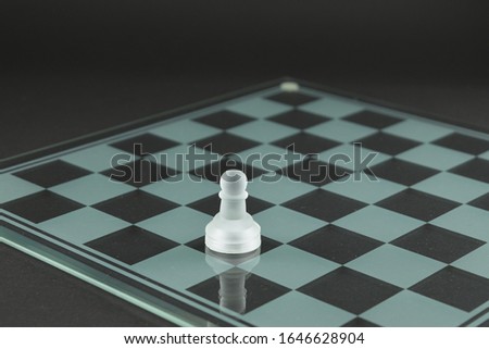 Glass chessboard and a chess pawn over a black background