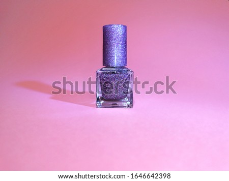 Bottle of nail polish with sparkles on a pink background.