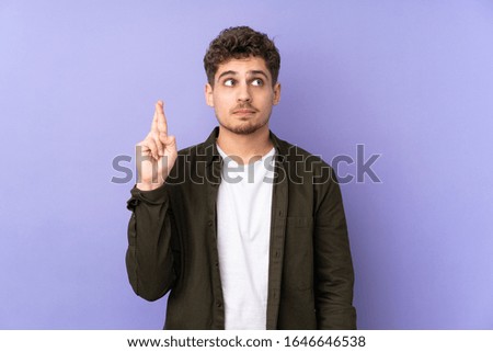 Caucasian man isolated on purple background with fingers crossing and wishing the best