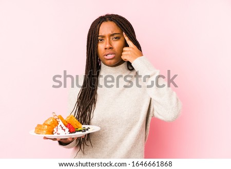 Young african american woman holding a waffle isolated showing a disappointment gesture with forefinger.