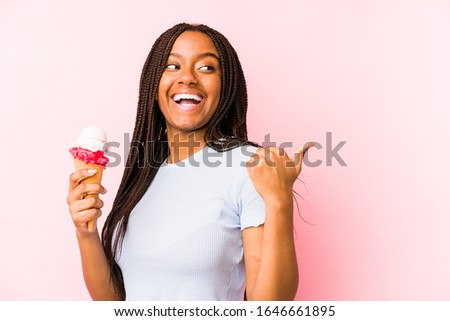 Young african american woman holding an ice cream isolated points with thumb finger away, laughing and carefree.