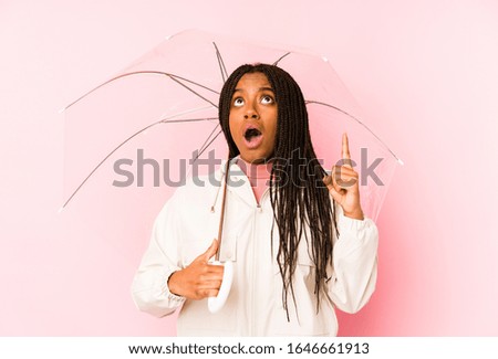 Young african american woman holding an umbrella isolated pointing upside with opened mouth.
