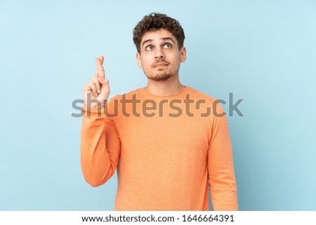 Caucasian man isolated on blue background with fingers crossing and wishing the best