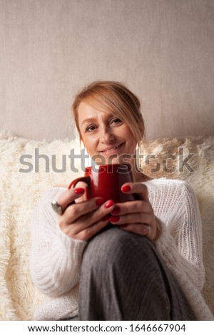 Portrait of an adult woman in a cozy room on the couch with a cup of tea / coffee.