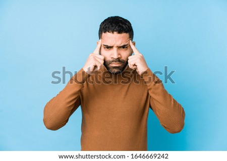 Young latin man against a blue  background isolated focused on a task, keeping forefingers pointing head.