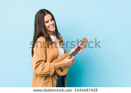 Young caucasian woman playing ukelele isolated on a blue background