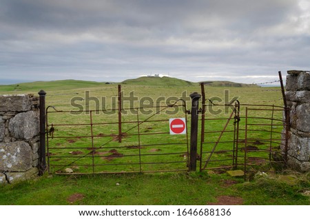 A rusty farm gate has a no entry symbol attached to it. Beside the gate is a rusty kissing gate. Both gates are topped with barbed wire. The location is on the Great Orme, Llandudno, North Wales, UK.